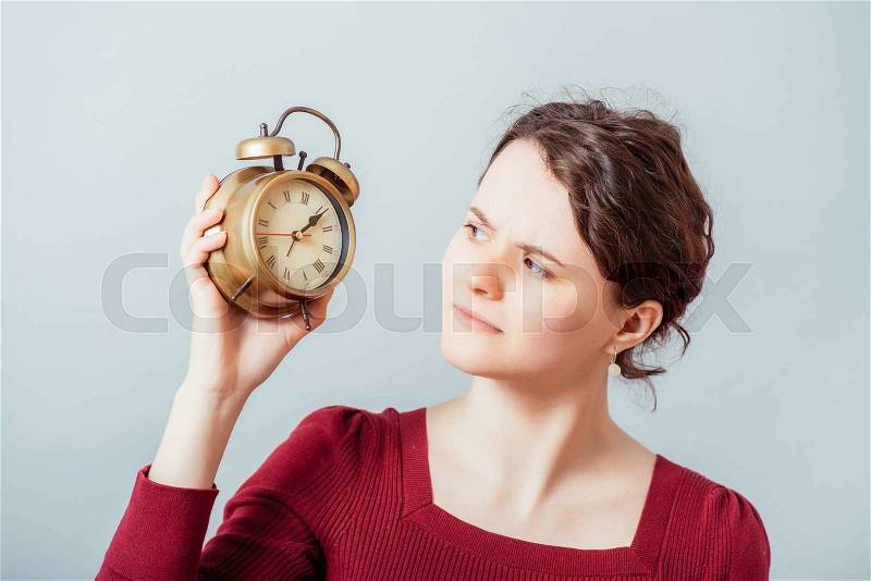 Woman showing an alarm clock. On a gray background, stock photo