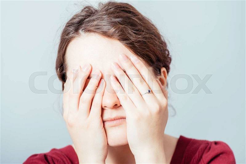 Young woman closes eyes with her hands, stock photo