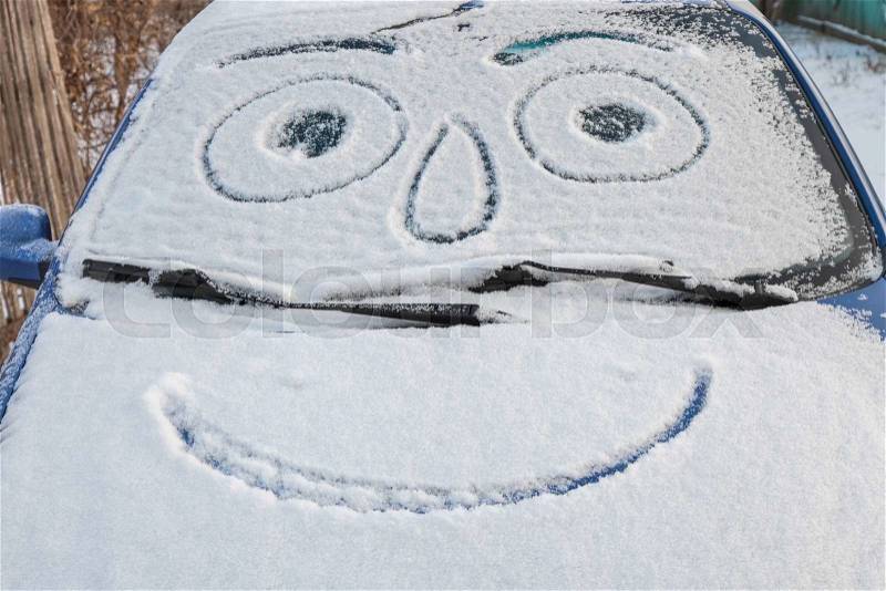 Snow-covered car with drawn smiley in windshield, stock photo