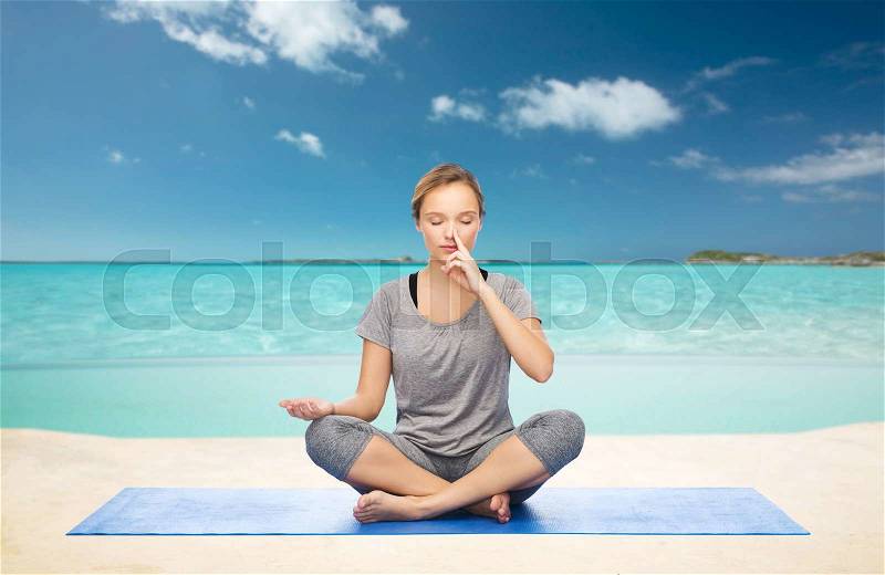 Fitness, sport, people and healthy lifestyle concept - woman making yoga meditation in lotus pose on mat over sea and sky background, stock photo