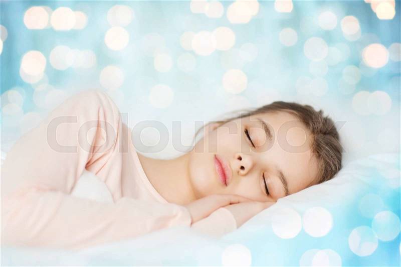 People, children, dreaming, rest and comfort concept - girl sleeping in bed over blue lights background, stock photo