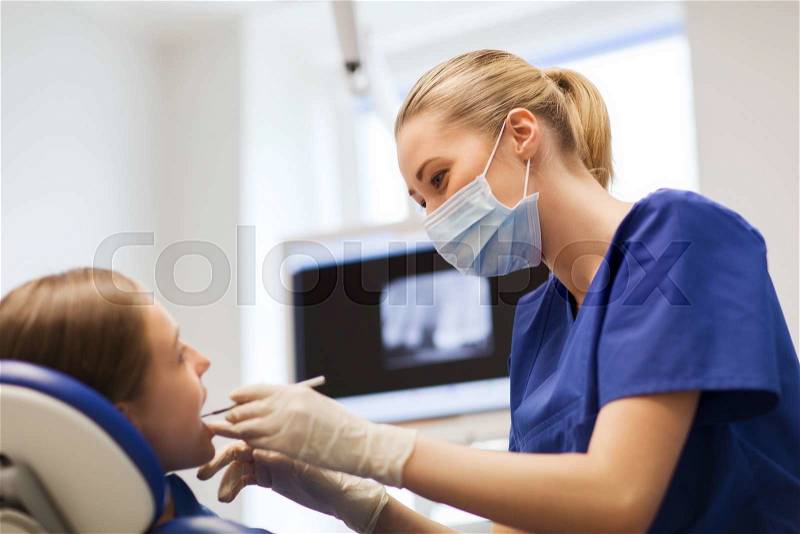 People, medicine, stomatology and health care concept - happy female dentist with mirror or dental probe checking patient girl teeth up at dental clinic office, stock photo