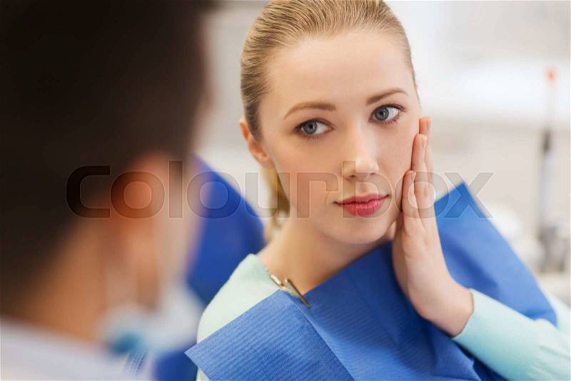 People, medicine, stomatology and health care concept - woman patient talking to male dentist and complain of toothache at dental clinic office, stock photo
