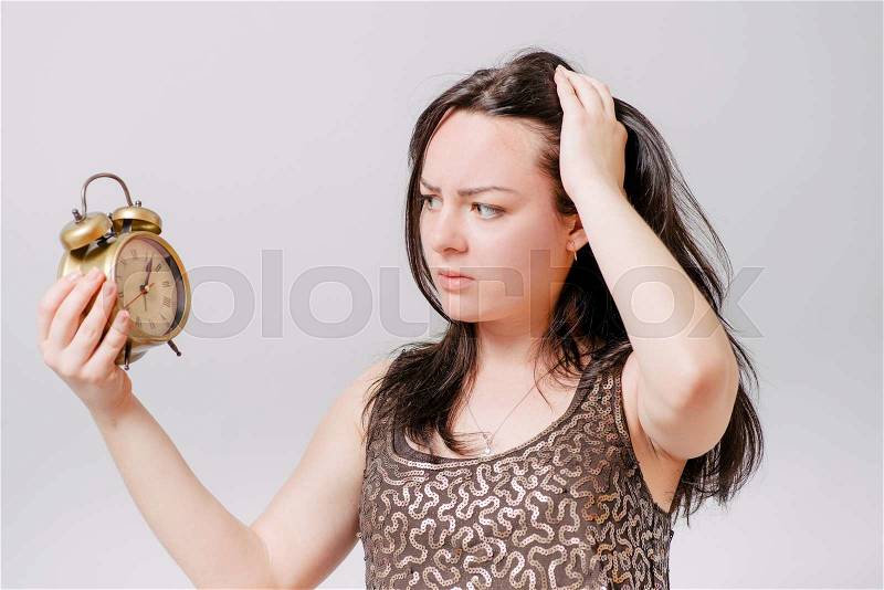 A woman looks at a wall clock with a hand on his head. On a gray background, stock photo