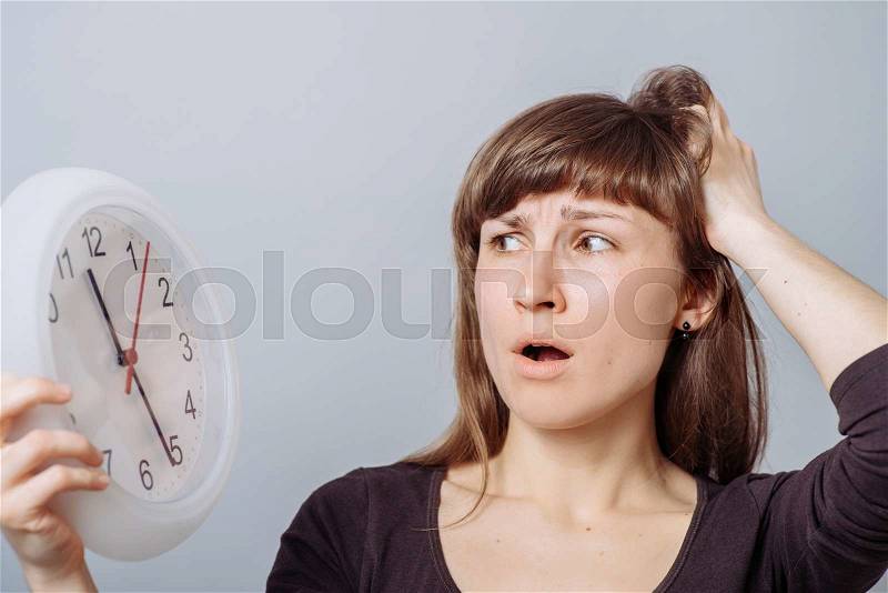 A woman looks at a wall clock with a hand on his head. On a gray background, stock photo