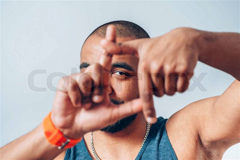 Smiling dark-skinned young man looking through a finger frame, stock photo