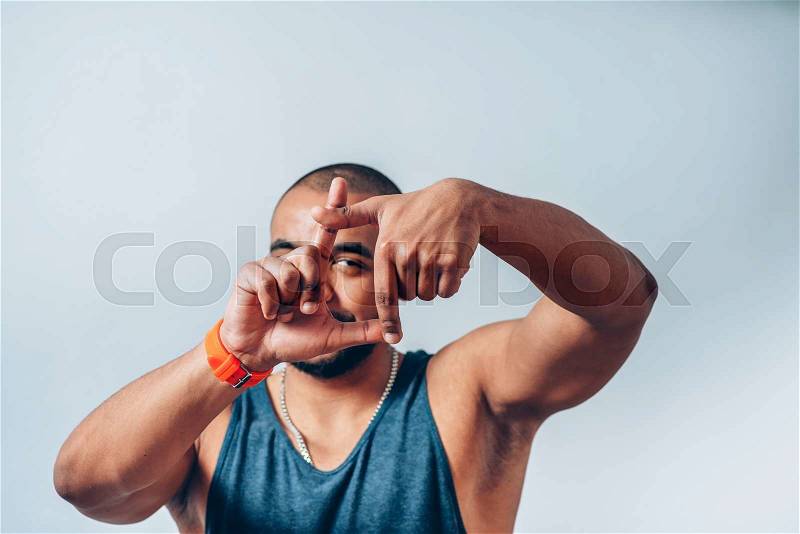 Smiling dark-skinned young man looking through a finger frame, stock photo
