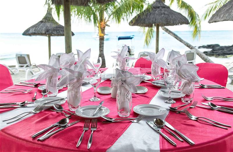 Romantic dinner on sunset beach. Festive pink table place setting. Selective focus, stock photo