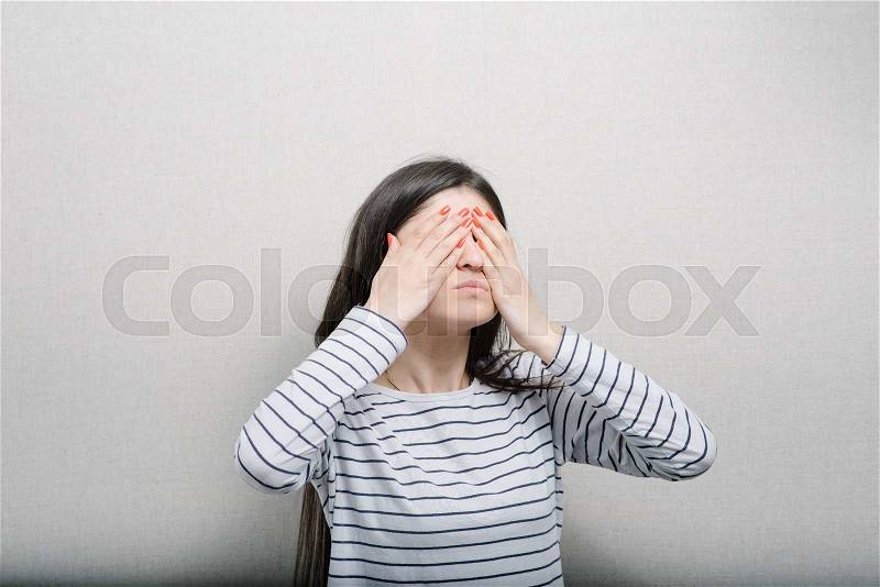 Beautiful brunette girl closes eyes with her hands, stock photo