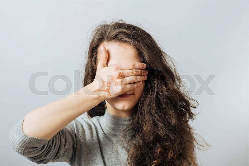 Young woman covering her eyes with her hand. On a gray background, stock photo