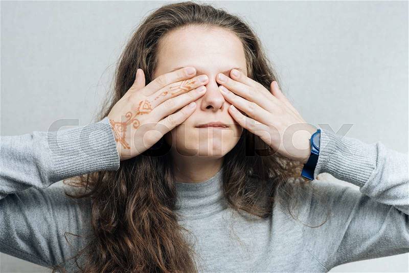Young woman covering her eyes with her hands. On a gray background, stock photo