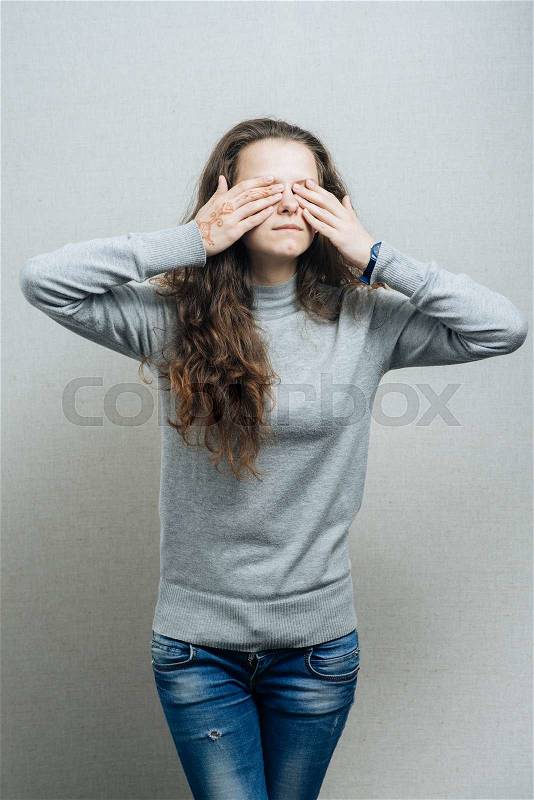 Young woman covering her eyes with her hands. On a gray background, stock photo