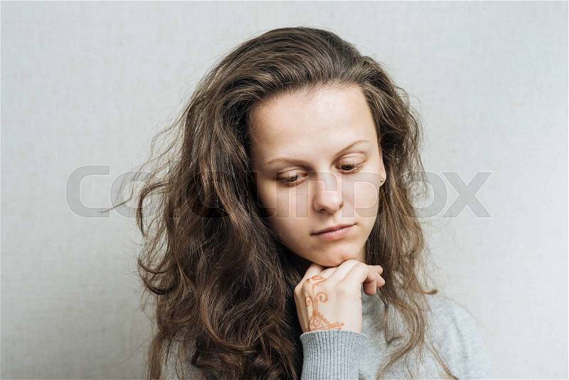 Young sad woman lowered her head. On a gray background, stock photo