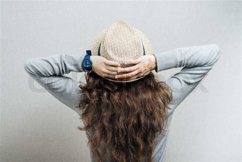A woman in a straw hat with hands on head, rear view. On a gray background, stock photo