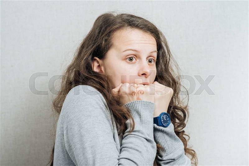 Woman afraid of biting fists. On a gray background, stock photo