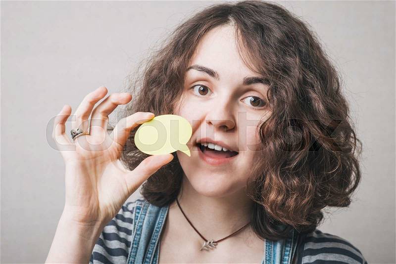 Woman holding a yellow sticker in front of her face, isolated on a gray background, stock photo