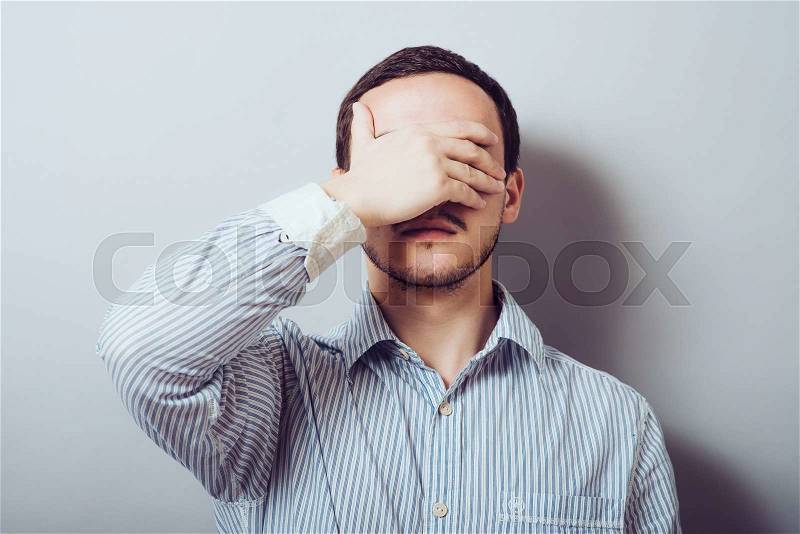 Stress, headache, health care and people concept - unhappy man covering his eyes by hand over gray background, stock photo