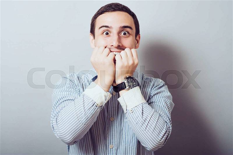 Young business man biting his nails while looking into the camera. on a light gray studio background, stock photo