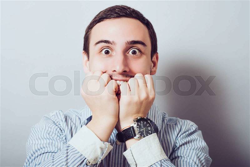 Young business man biting his nails while looking into the camera. on a light gray studio background, stock photo