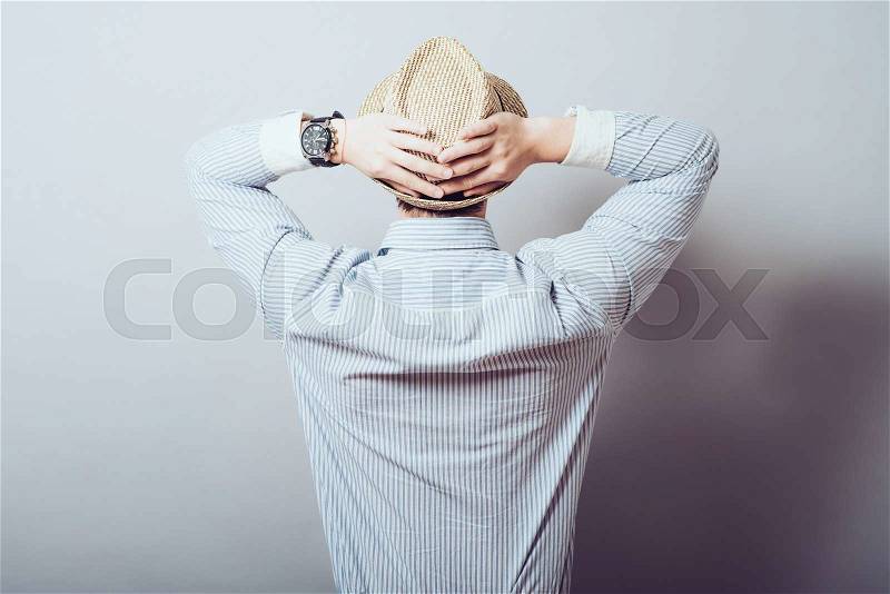 The man in the hat put his hands behind his head, rear view. Gray background, stock photo