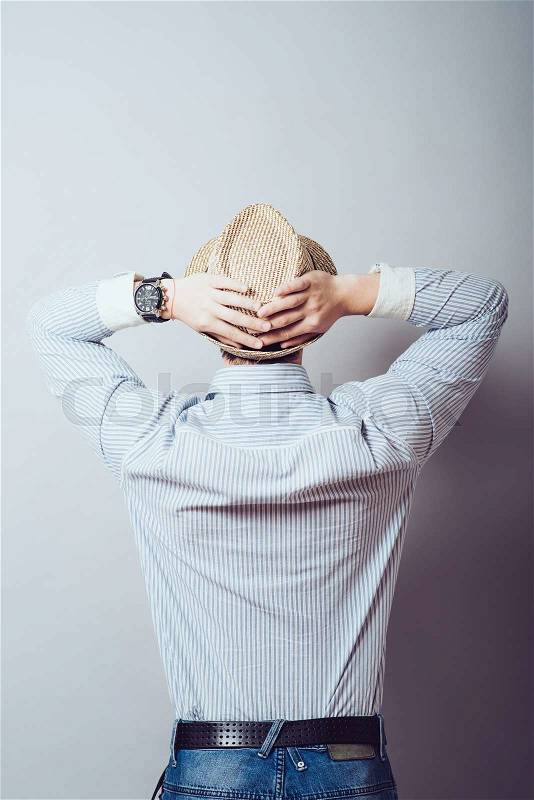 The man in the hat put his hands behind his head, rear view. Gray background, stock photo