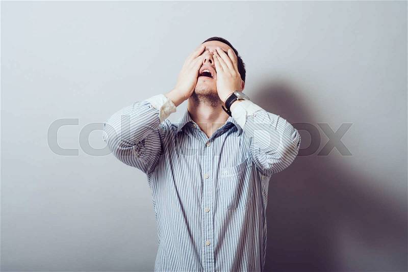 Man screaming mouth open, keep your head arm, wearing a casual blue shirt, isolated gray background, the concept of facial emotions, stock photo