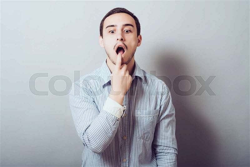 Male of European appearance causes vomiting putting his fingers in his mouth on a gray background, nausea, stock photo