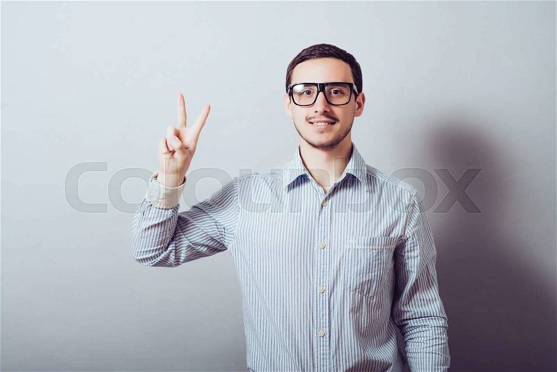 The man in the glasses shows victory gesture . On a gray background, stock photo