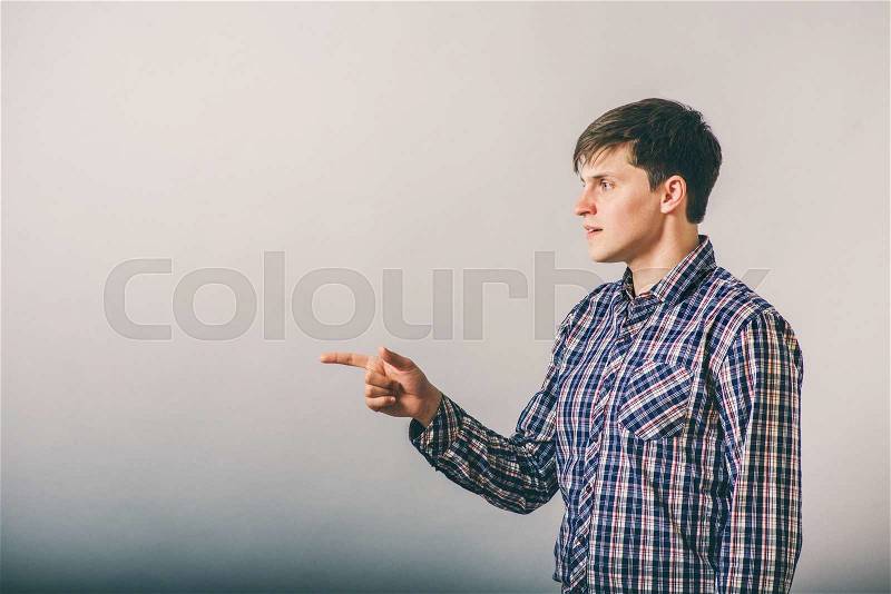 Closeup side view portrait of young man, pointing with finger at someone or something, stock photo
