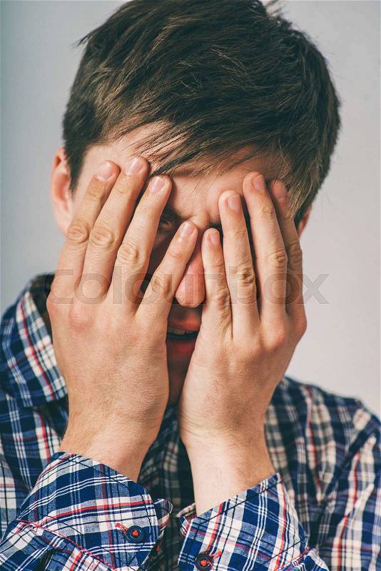 Stress, headache, health care and people concept - unhappy man covering his eyes by hand over gray background, stock photo