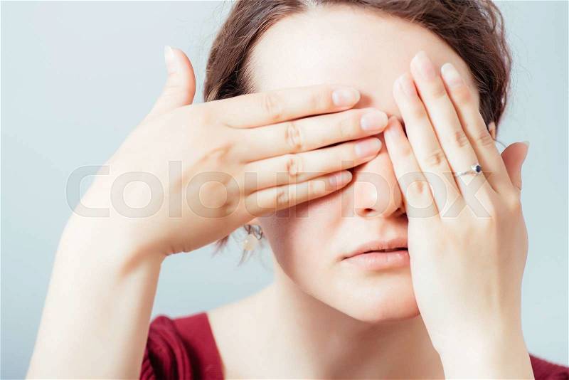 Young woman covering her eyes with her hand. On a gray background, stock photo