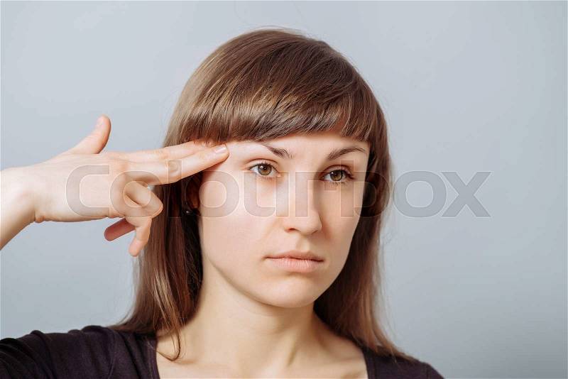 The woman making the gesture of suicide, the index finger to his temple, an imaginary gun. Gray background, stock photo