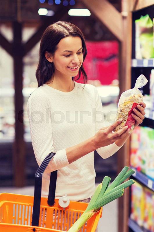 Sale, shopping, consumerism and people concept - happy young woman with food basket choosing muesli in market, stock photo