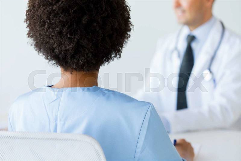 Profession, people and medicine concept - close up of african female doctor or nurse at conference in hospital from back, stock photo