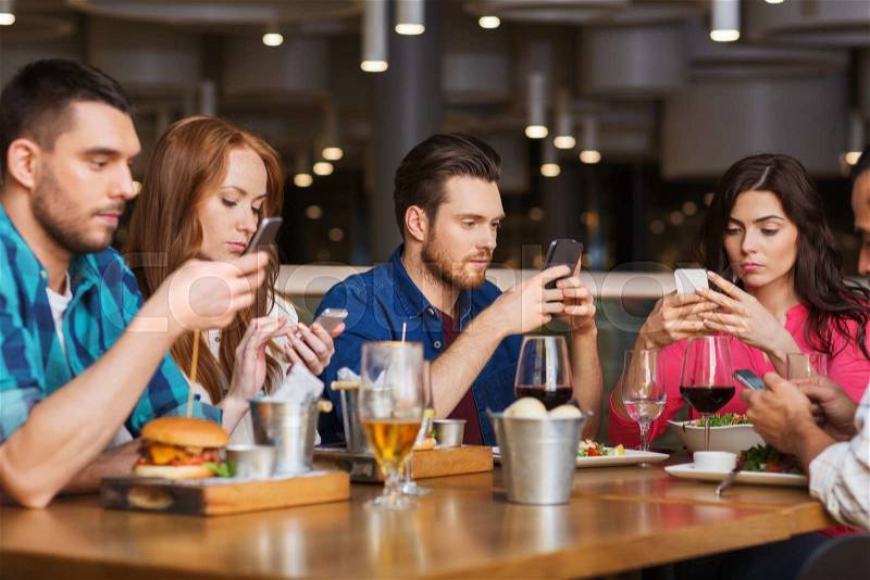 Leisure, technology, lifestyle and people concept - friends with smartphones dining at restaurant, stock photo