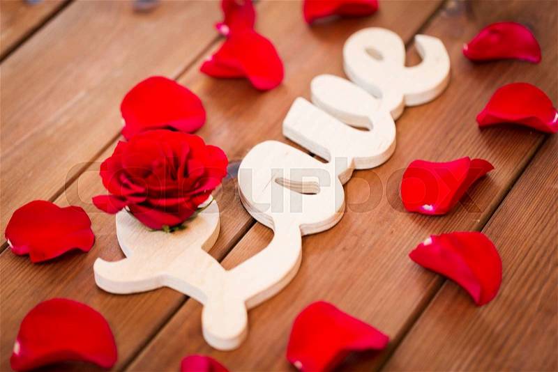Love, date, romance, valentines day and holidays concept - close up of word love cutout with red rose petals on wood, stock photo