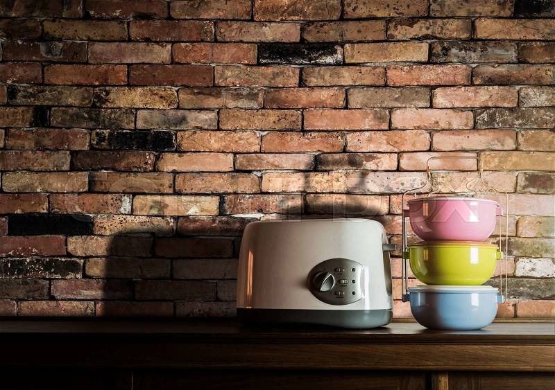 Colorful tiffin carrier and toaster on wooden cupboard with vintage brick wall background against warm light, stock photo
