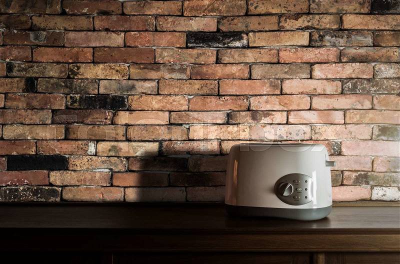 White toaster on wooden cupboard in kitchen room with vintage brick wall against warm light, stock photo