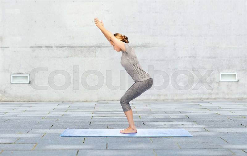 Fitness, sport, people and healthy lifestyle concept - woman making yoga in chair pose on mat over urban street background, stock photo