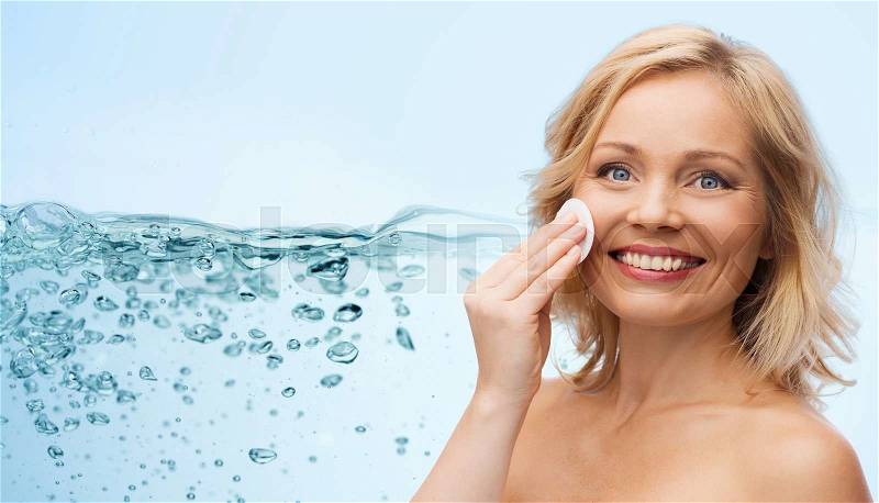 Beauty, people and skincare concept - happy middle aged woman cleaning face and removing make up with cotton pad over water splash with air bubbles background, stock photo
