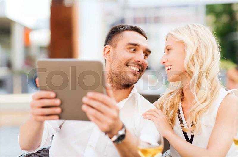 Love, dating, people, technology and holidays concept - happy couple with tablet pc computer talking at restaurant lounge or terrace, stock photo