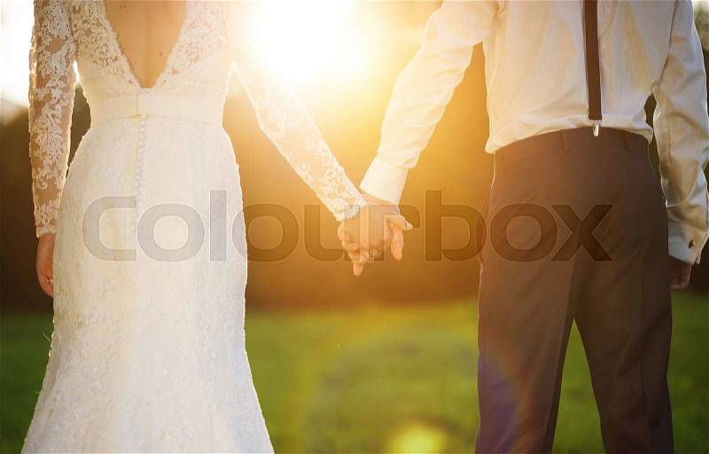 Young wedding couple holding hands as they enjoy romantic moments outside on a summer meadow, stock photo