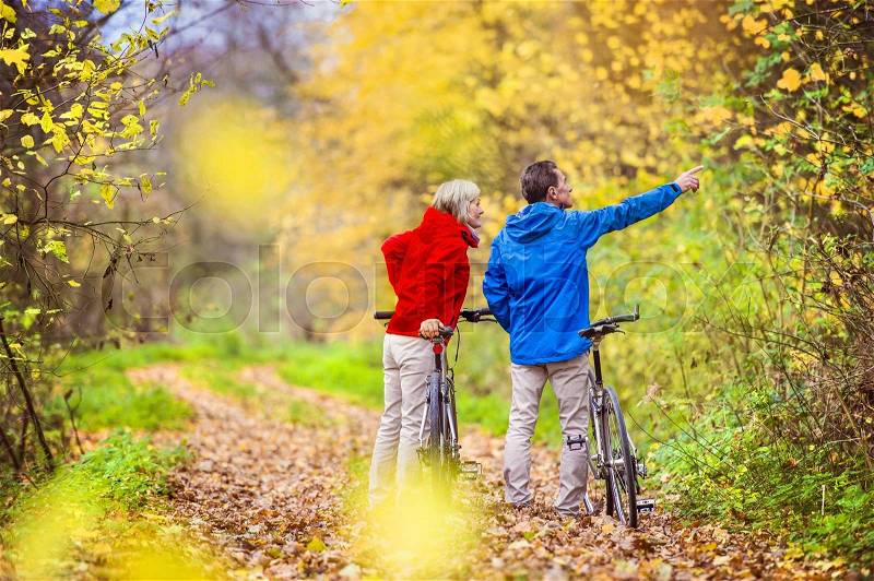 Active seniors having walk with bike in autumn nature. They having romantic time outdoor, stock photo