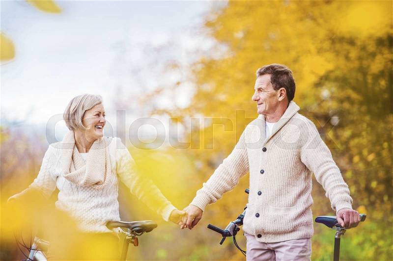 Active seniors riding bikes in autumn nature. They having romantic time outdoor, stock photo