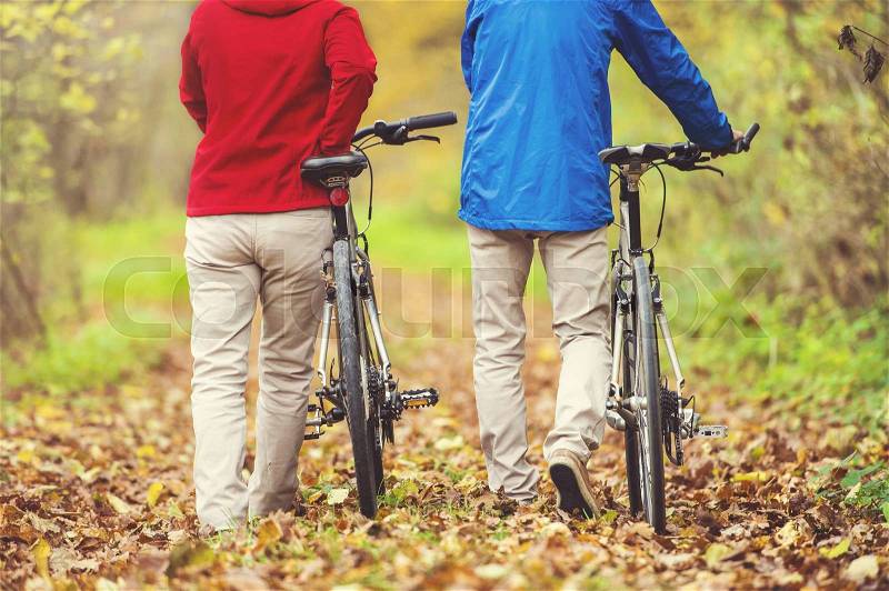 Unrecognizable active seniors having walk with bike in autumn nature. They having romantic time outdoor, stock photo