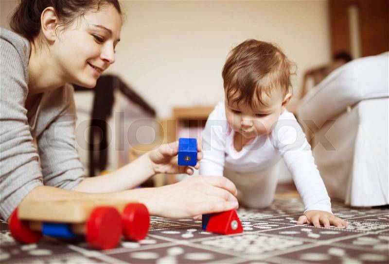 Cute little baby girl playing with her mother on a carpet in a living room, stock photo