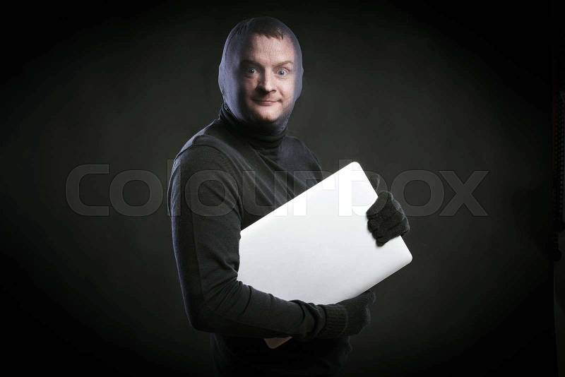 Thief in action with balaclava on his face, dressed in black. Studio shot on black background, stock photo