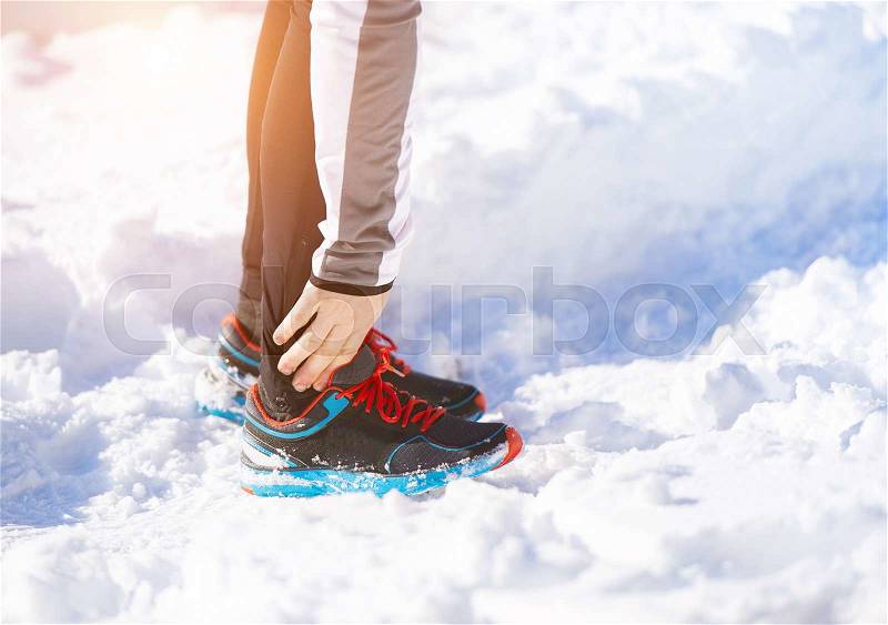 Injury of a young sportsman jogging outside in sunny winter park, stock photo