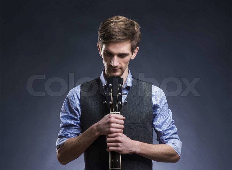 Young handsome guitar player. Studio shot on black background, stock photo
