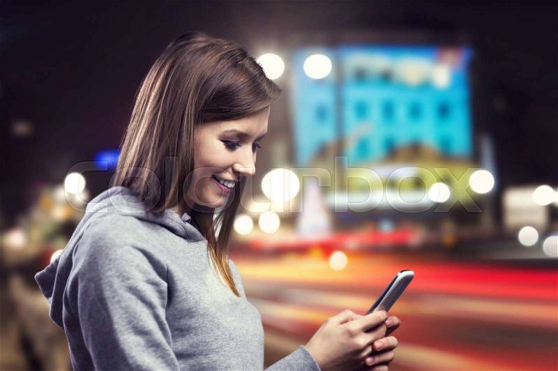 Young woman jogging at night in the city with her smart phone, stock photo